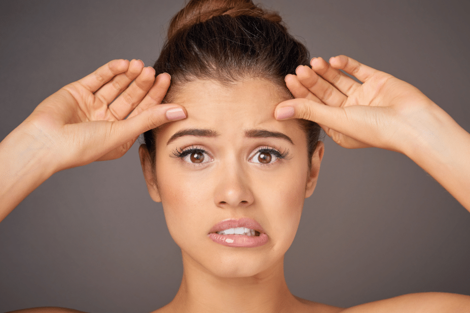 A young woman checking her forehead skin with a doubtful expression on her face
