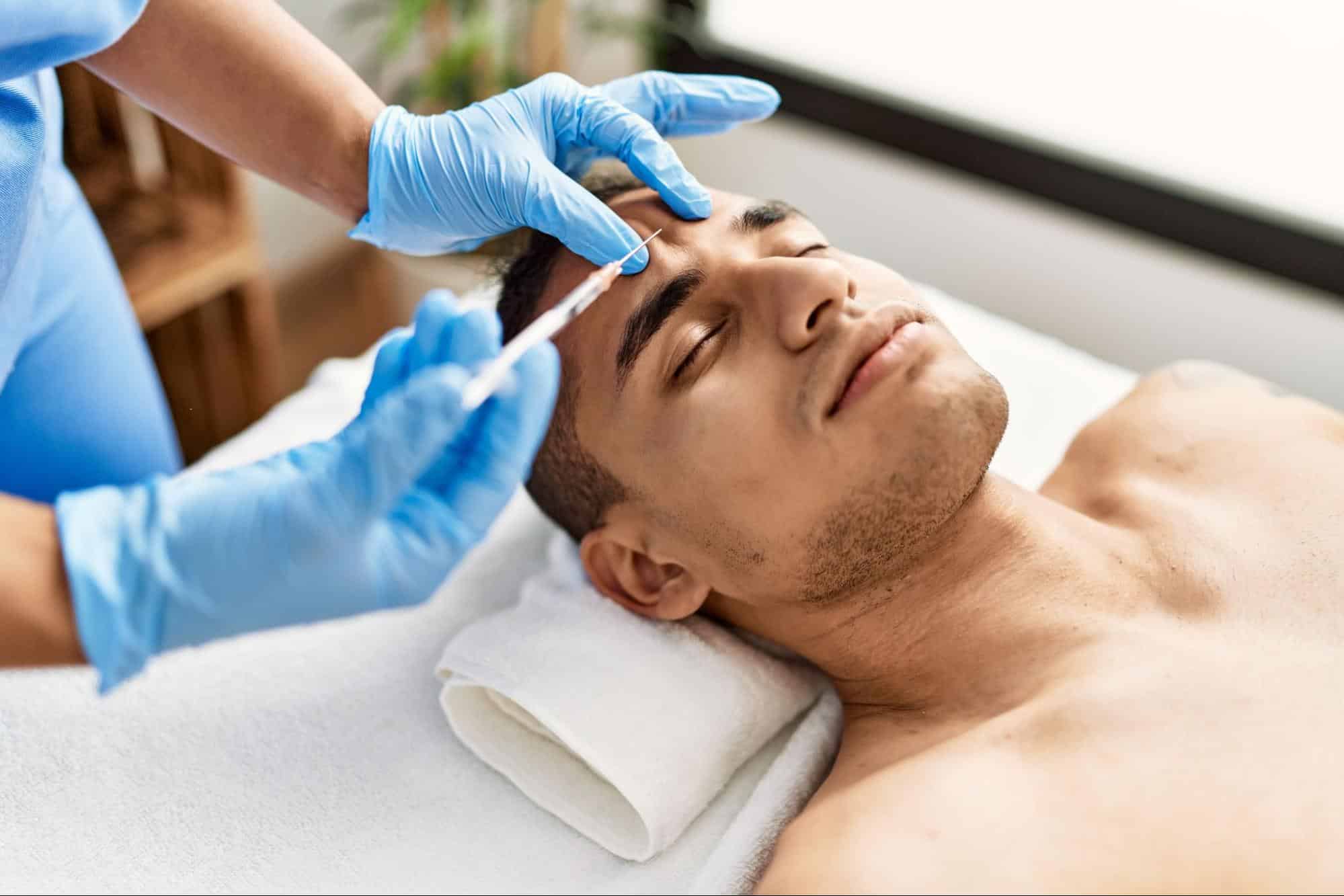 A man lying on a towel receiving an injection from an esthetician.
